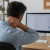 Personne en télétravail souffrant de douleurs cervicales devant son ordinateur