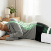 Démonstration de la meilleure position pour dormir avec une sciatique : femme sur le côté avec oreiller ergonomique cervical OrthoDodo et oreiller de genoux pour aligner le bassin et décompresser le nerf sciatique. Indicateurs techniques verts montrant l'alignement de la colonne vertébrale.